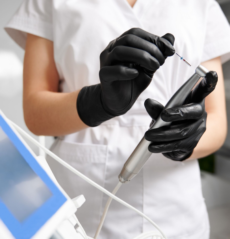 Dental professional wearing black gloves inserting a tool into a handpiece, preparing equipment for a procedure.