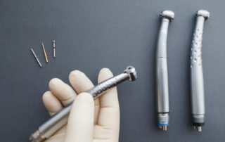 A handpiece repair technician holds a handpiece next to other handpieces and parts.