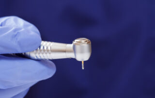 A close-up image of the head of a dental handpiece in a blue gloved hand.