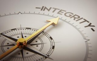 An extreme close-up of a compass with its’ arrow pointing to the word “integrity”.