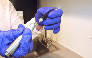 A technician uses a handpiece oil dropper to lubricate a handpiece during maintenance.